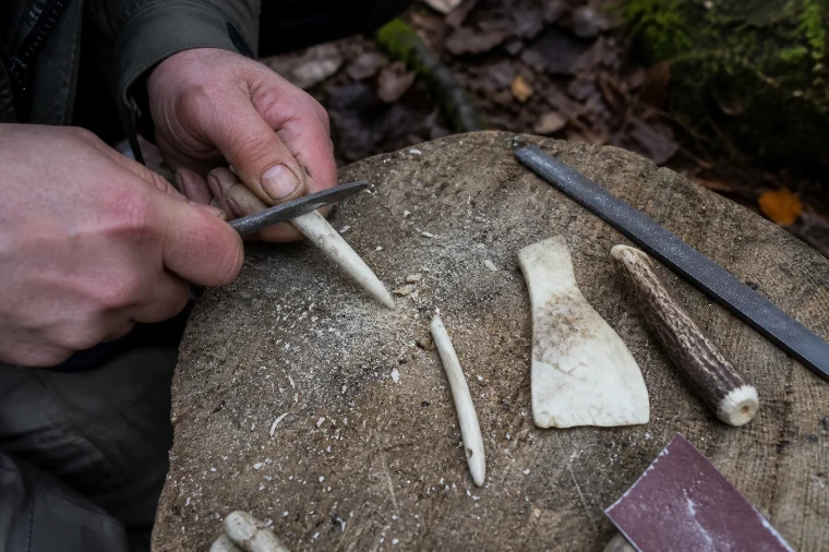 Hände feilen eine Knochenspitze neben Knochennadel, Schaber und Geweihstück