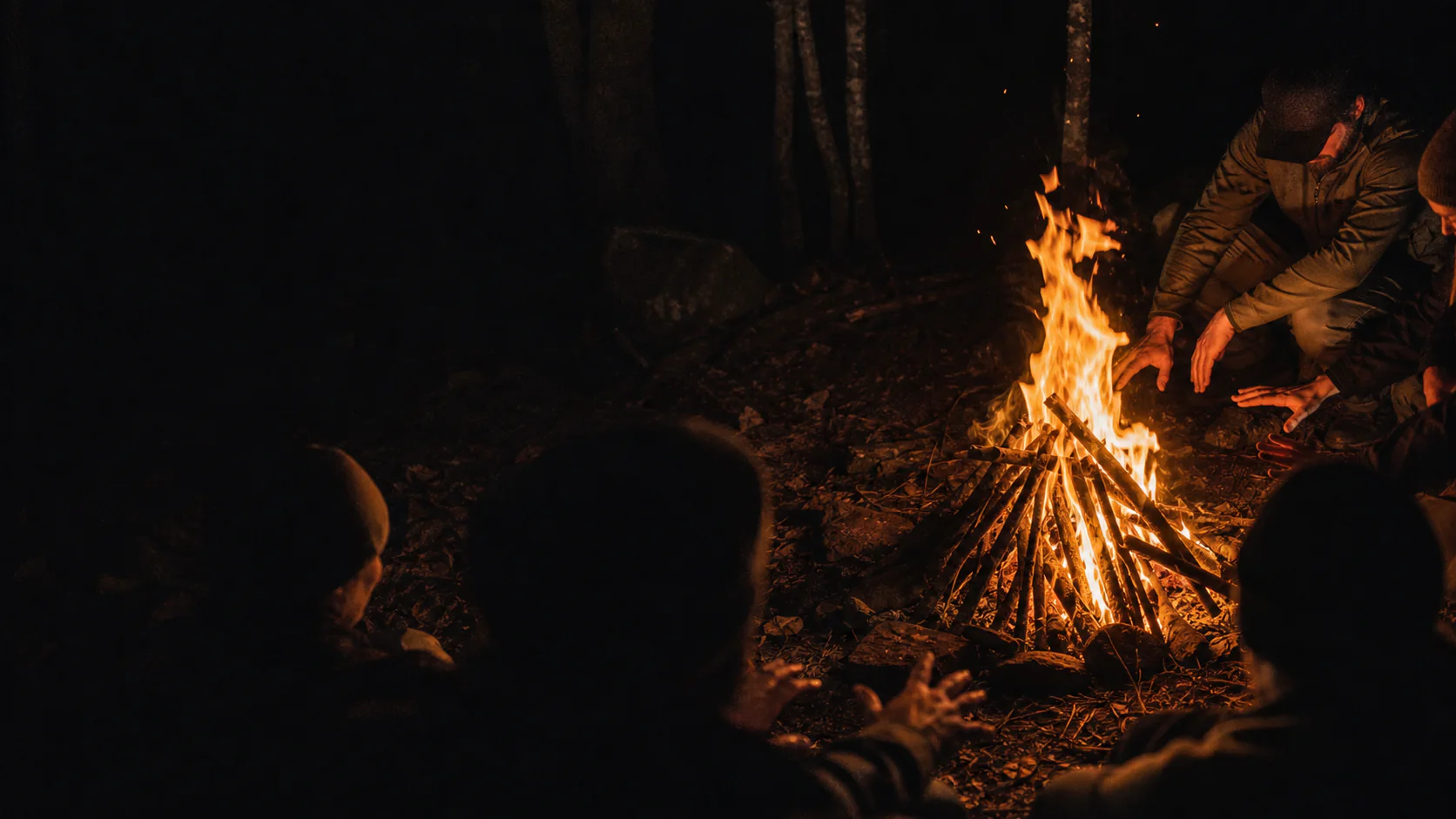 Teilnehmer wärmen sich nachts am Lagerfeuer während der Survival Guide Ausbildung im Schwarzwald
